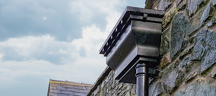 Black ornate aluminium hopper head mounted to stone wall