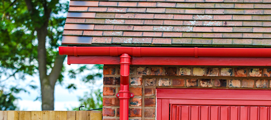 Aluminium red half round guttering with traditional cast round downpipes fitted to outbuilding at Garston Barns